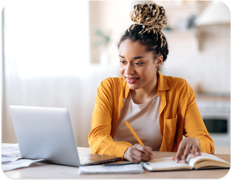 woman writing in notebook while looking at laptop
