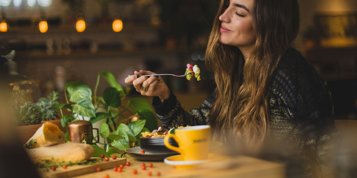 A young woman with long, brown hair closes her eyes while holding a forkful of food.