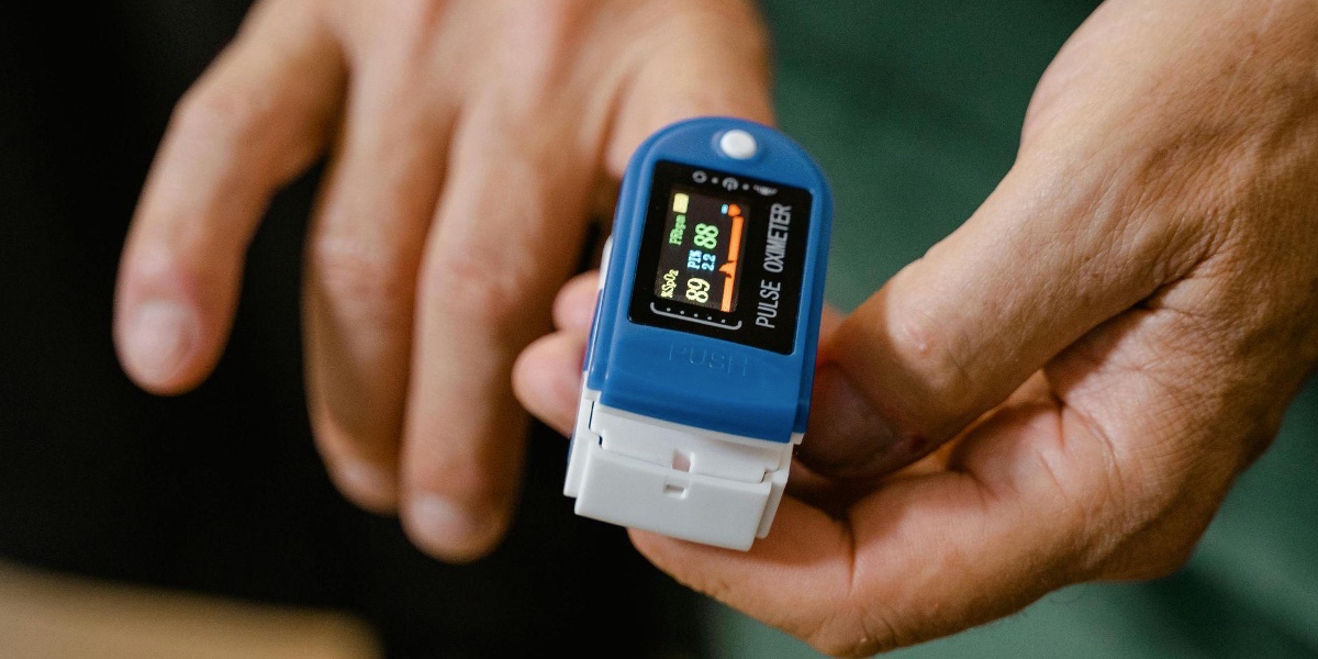 In a close-up of human hands, a person uses a medical device on a finger.