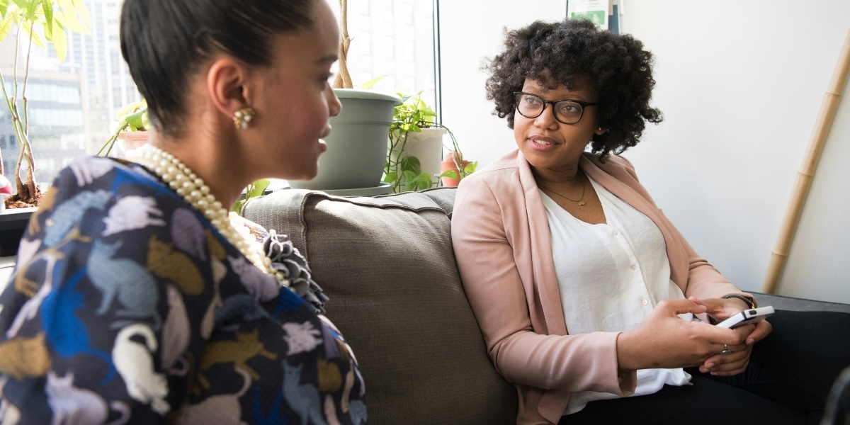 Two women sitting on a couch talking.